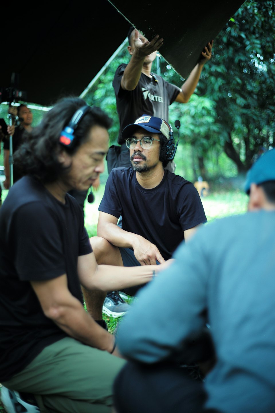 Film crew members working outdoors among green foliage.
