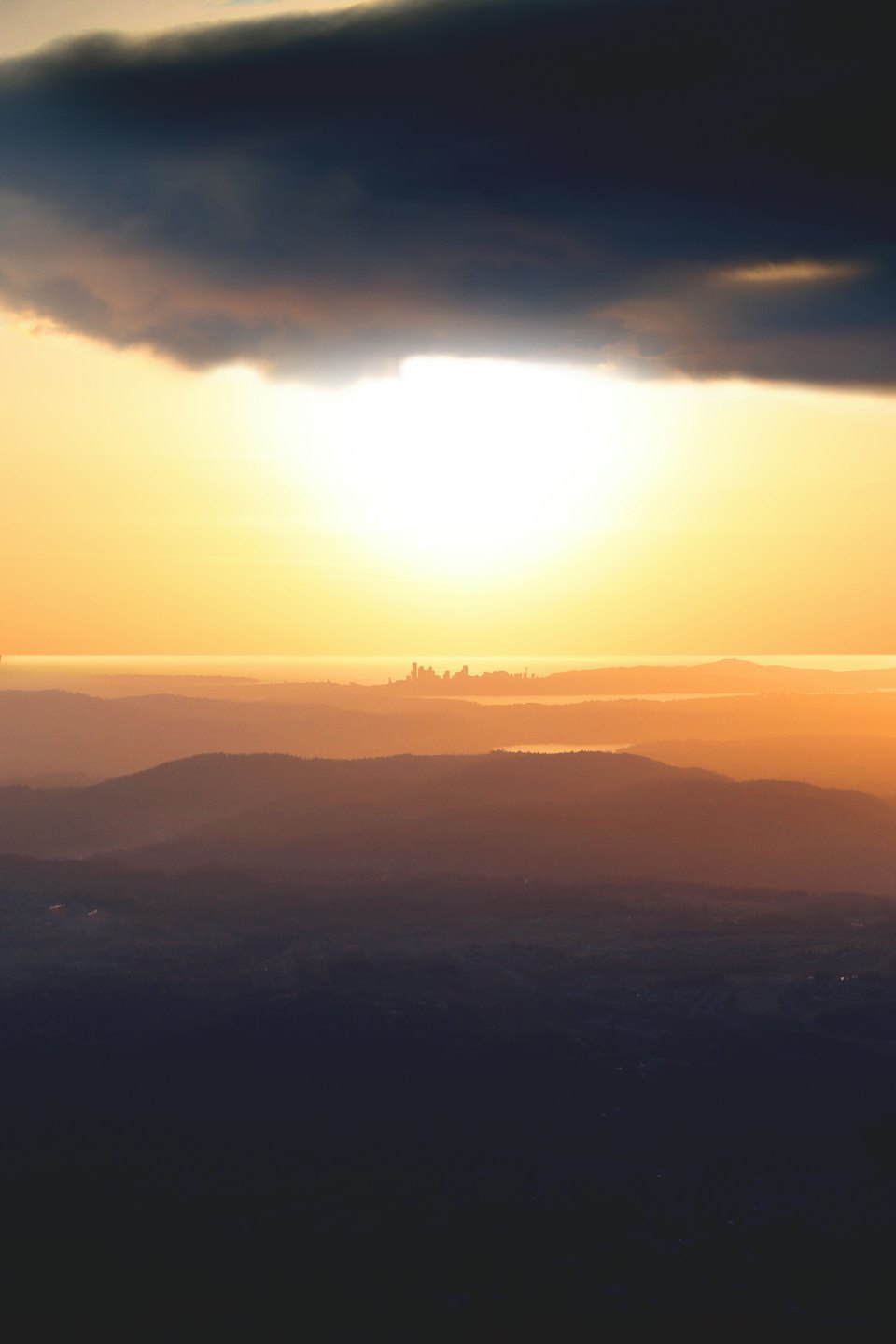 Distant city skyline silhouetted against layered hills at sunset.
