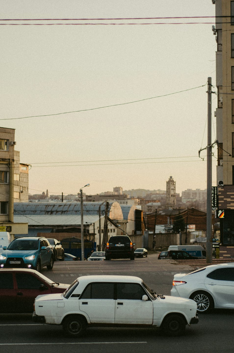 Cars drive through a busy city street with industrial buildings.