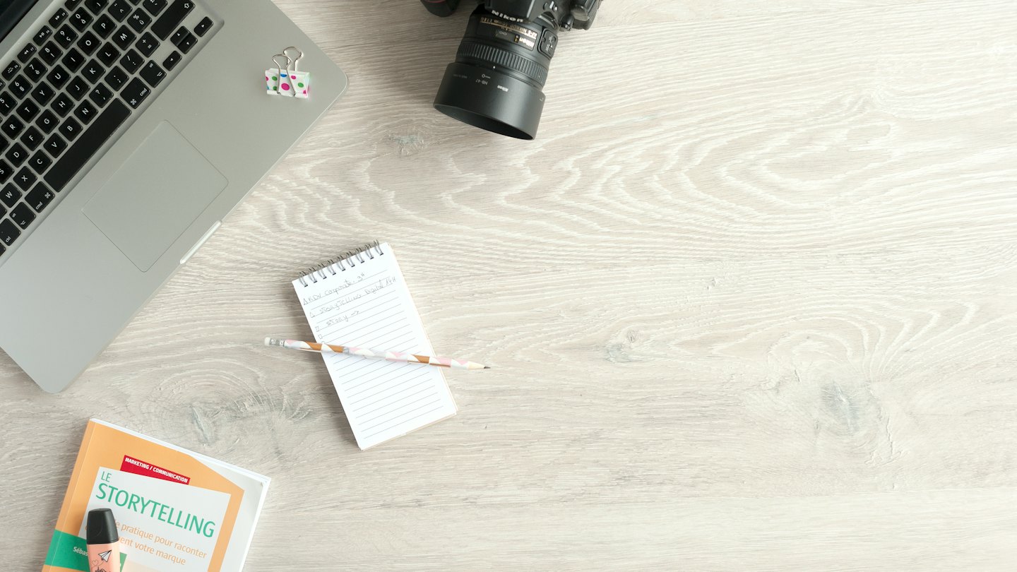 Laptop, camera, and book on a wooden desk.