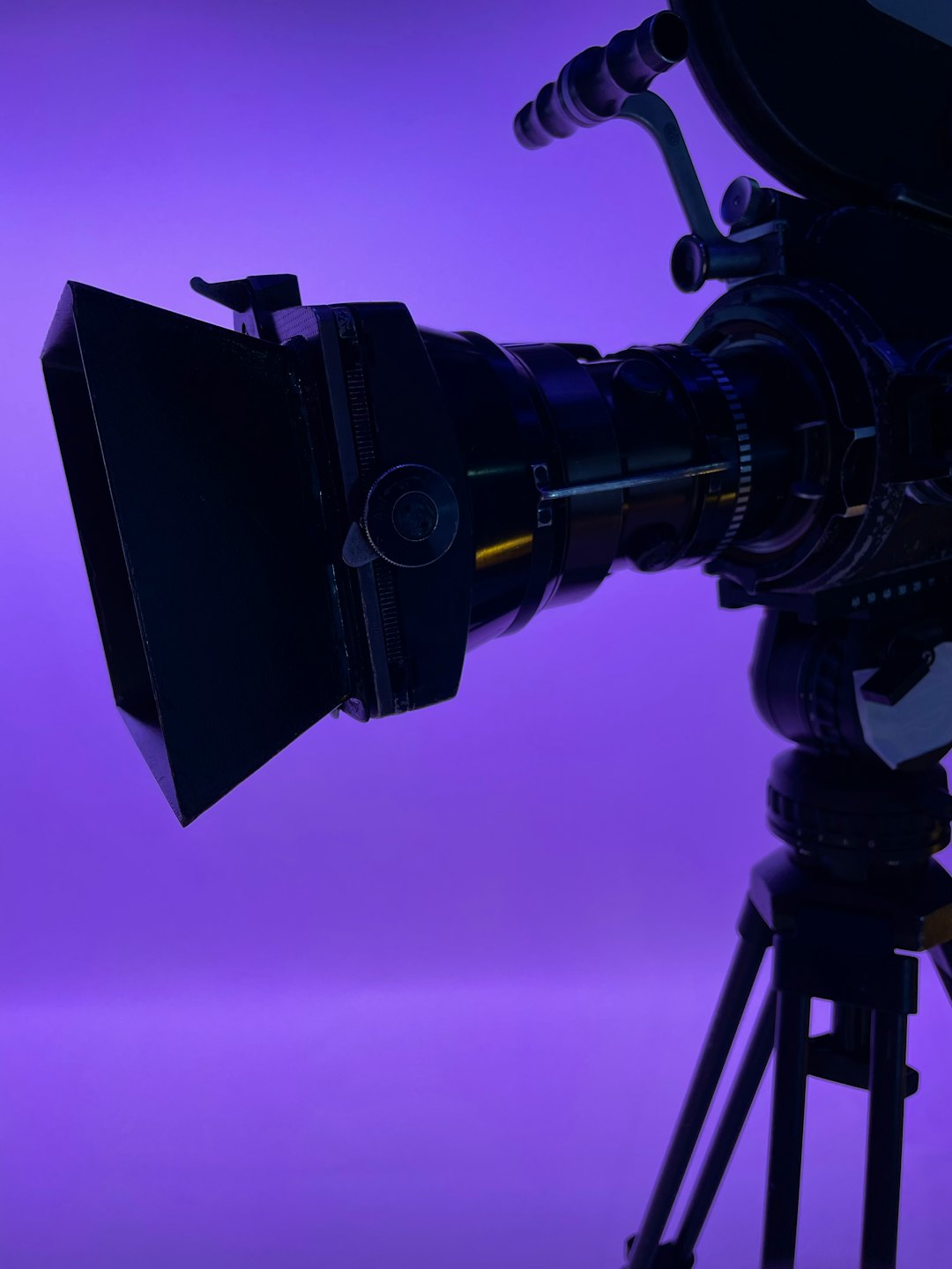 Vintage film camera on tripod against a bright purple background.
