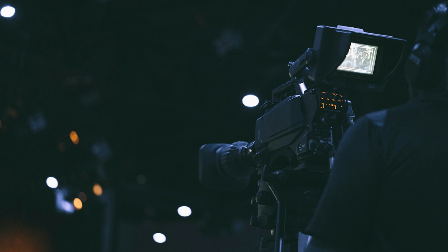 Person operating a video camera with glowing orange controls.