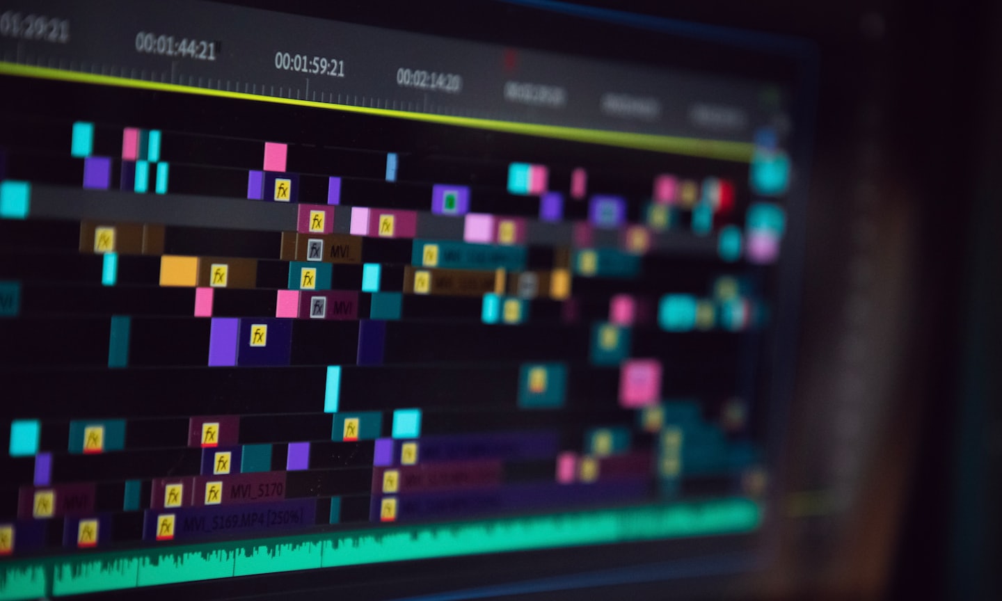 Video editing timeline with colorful clips and time codes on a screen.